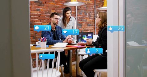 Startup team collaborating around laptop with social media engagement overlays in brick office