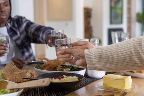Friends clinking glasses over home dinner featuring roasted chicken and garnished water