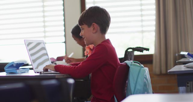 Portrait of diverse schoolchildren sitting in classtoom, using laptop, looking at camera, smiling. children at primary school