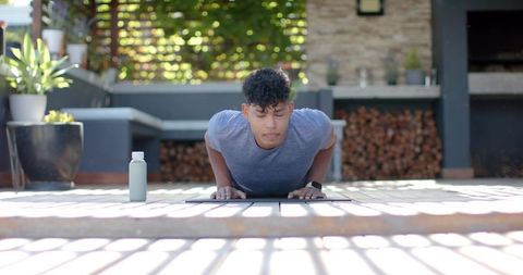 African american man performing push-ups on sunlit backyard deck for home fitness training