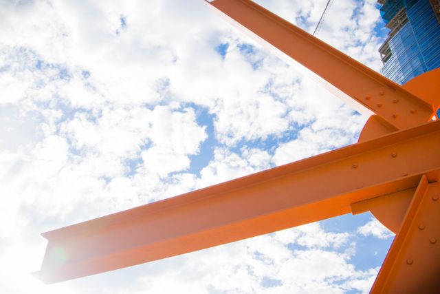 Bright orange steel beams stretch toward a cloudy sky, emphasizing strength and modern architecture. This image is ideal for promoting construction companies, engineering courses, architectural projects, or illustrating industry-related articles and advertisements.