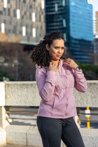 Young woman adjusting pink zip-up jacket on urban bridge, smartwatch on wrist