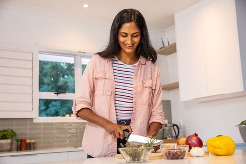 Indian woman chopping fresh herbs on cutting board in bright modern kitchen smiling