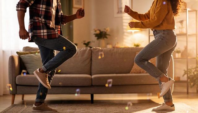 Dancing couple mirroring steps in sunlit living room with denim sneakers and bubbles