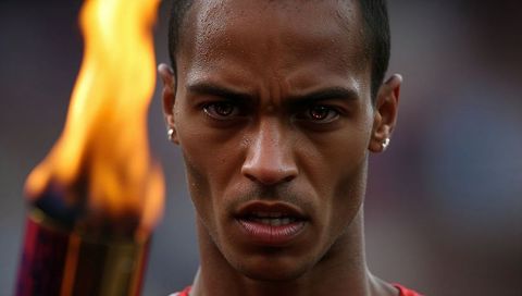Focusing male athlete holding flaming torch closeup, intense concentration at stadium