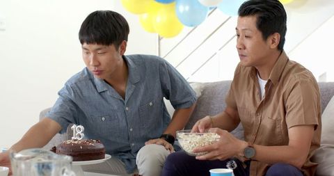 Asian Father and Son Celebrating with Snacks and Cake Indoors