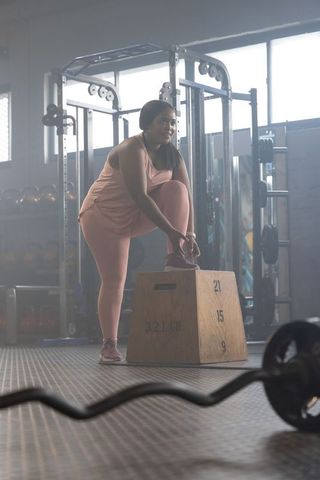 African american woman tying shoelace on plyo box wearing pink activewear preparing for workout
