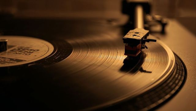 Warm amber vinyl turntable close-up showing stylus on spinning record with nostalgic glow