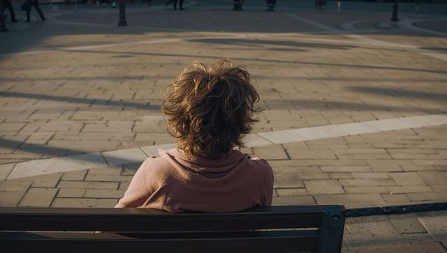 Solitary man sitting on bench overlooking sunlit urban plaza with long shadows