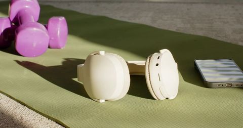 Cream wireless headphones resting on green yoga mat with purple dumbbells and smartphone
