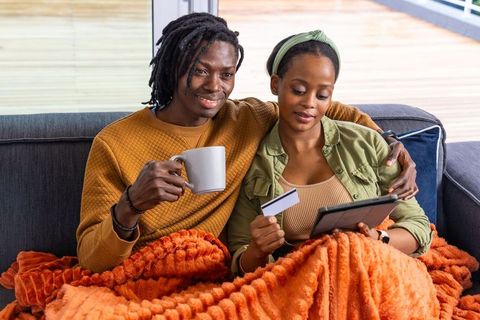 African american couple shopping online on tablet while relaxing under orange blanket