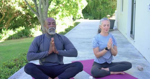 Diverse couple practicing outdoor yoga meditation on patio mats, smartwatch visible