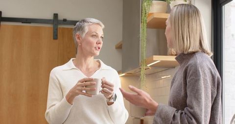 Mature and middle-aged friends chatting over coffee in bright modern kitchen