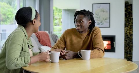 African American couple sharing coffee and chatting by cozy fireplace at home