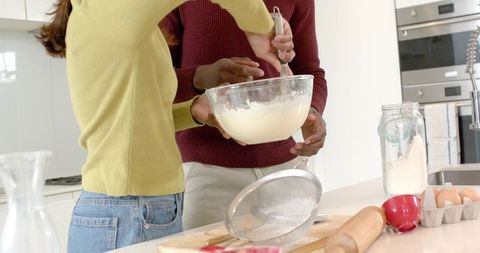 Multicultural couple whisking batter on modern kitchen island baking together with flour and eggs