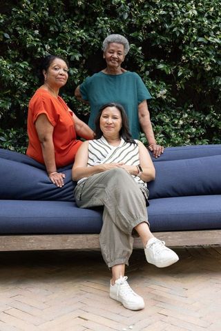 Multigenerational women relaxing on deep blue patio sofa amid lush greenery with casual sneakers