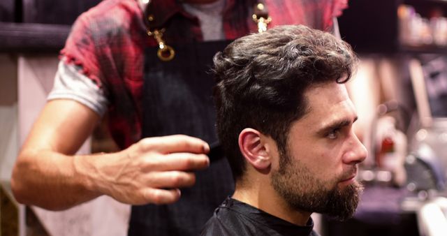 Modern barber applying final touches to client's haircut in a stylish barber shop. Perfect for content related to men's grooming, hair care services, male fashion, and small businesses. Could be used in advertisements for hair salons, barber training materials, or lifestyle magazines.