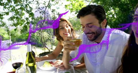 Smiling friends enjoying wine and laughter at sunlit garden brunch with purple overlay