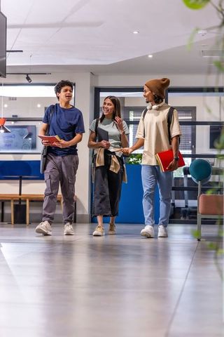 Diverse students walking and talking in modern campus lobby with notebooks and backpacks