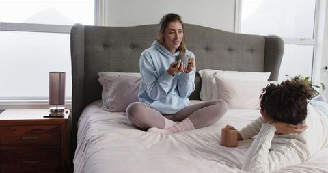 Cozy Morning Conversation: Female Friends Relaxing on Bed Sharing Coffee