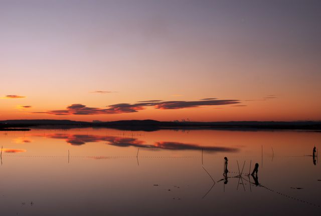 Tranquil sunset reflecting over calm lake with silhouettes of fishermen - Download Free Stock Photos Pikwizard.com