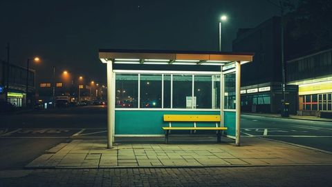 Illuminated bus shelter at night with yellow bench