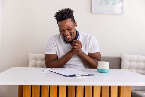 African american man smiling while filling paperwork at minimalist home table with ceramic cup