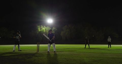 Night cricket batter at stumps under floodlight wearing helmet and pads preparing shot