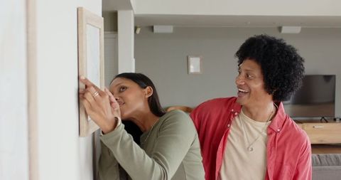 Diverse couple arranging picture frame in cozy living room