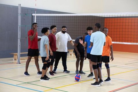 Diverse male volleyball team huddling around red-blue ball on indoor gym court