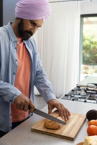 Man in kitchen cutting rustic bread on wooden cutting board