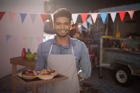 Smiling Vendor Serving Fruit Bowls at Outdoor Market
