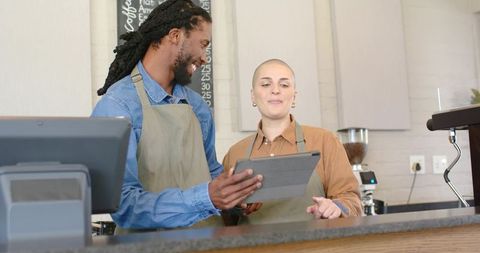 Baristas collaborating with tablet behind cafe counter, training and friendly service