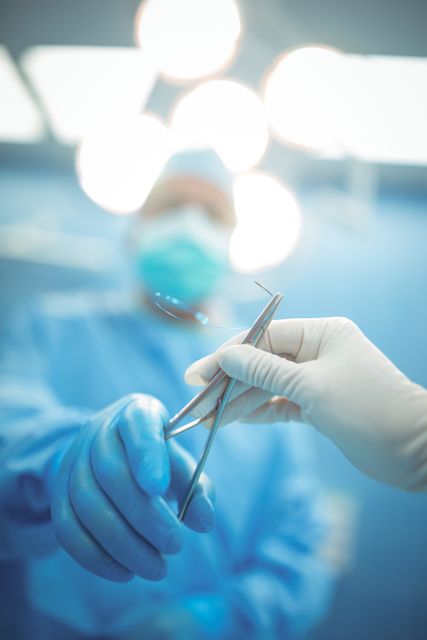 Surgeon passing a surgical tool to a colleague in an operation theater, emphasizing teamwork and precision in a sterile environment. Ideal for use in medical articles, healthcare websites, surgical procedure guides, and hospital promotional materials.