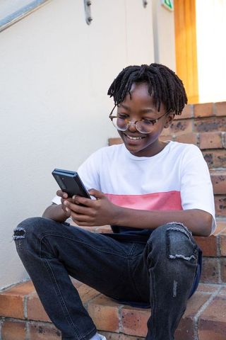 Smiling Teenage Boy Using Smartphone on Brick Steps