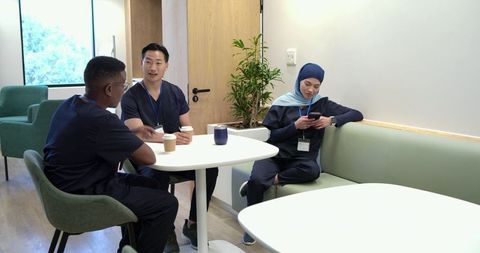 Diverse healthcare team taking coffee break and collaborating in modern staff lounge