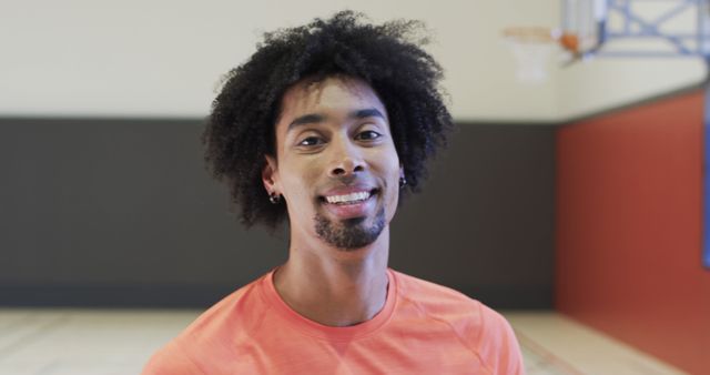 Young athletic man with afro hair smiling in an indoor gymnasium. Ideal for use in fitness, sports, and health-related promotions. Suitable for illustrating youth, vitality, and active lifestyle concepts.