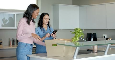 Two Female Friends Unpacking Groceries in Modern Kitchen