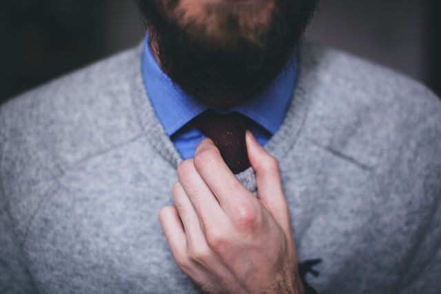 Close-up view of a man adjusting his tie while wearing a sweater over a collared shirt. Ideal for illustrating business casual attire, men's fashion, personal style, and professional preparation.