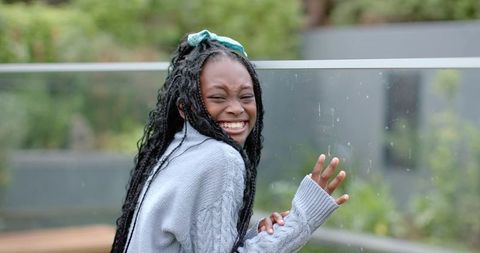 Joyful african american girl laughing and touching glass on balcony with braids