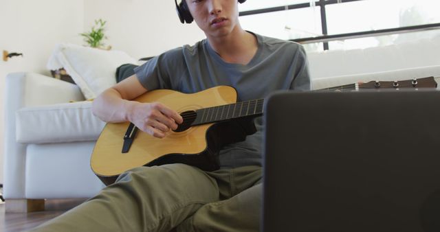 Asian boy wearing headphones playing guitar looking at the laptop at home. teenager lifestyle and living concept
