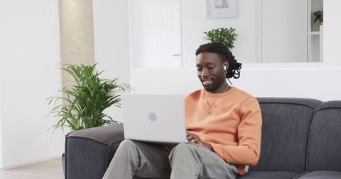African American man working remotely on laptop in minimalist living room with earbuds