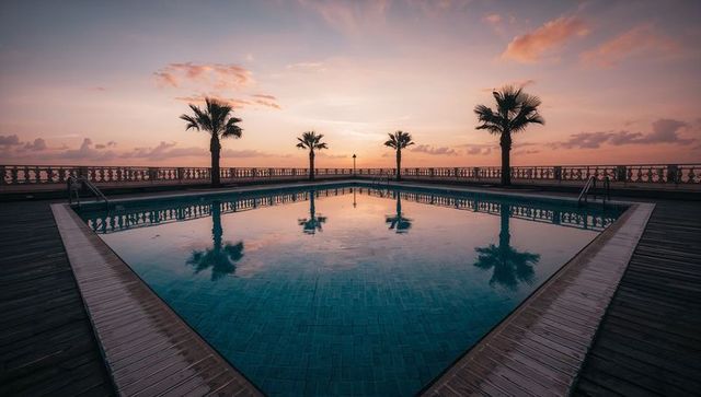 Reflecting pool mirroring palm trees at pastel sunset over calm ocean horizon