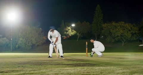 Playing night cricket under floodlights with batsman defending crease and wicketkeeper