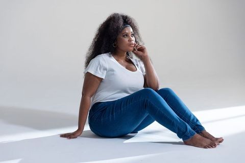 Serene african american woman sitting barefoot in jeans and white tee looking thoughtful