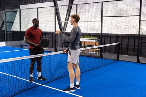 Diverse male padel players discussing strategy at net on vibrant indoor blue court