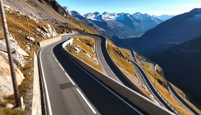 Winding alpine pass road descending serpentine switchbacks with snow-capped mountains