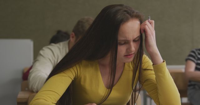 Young female student experiencing stress while taking an exam. Ideal for depicting educational challenges, student life, test-taking anxiety, and school-related stress. This can be used in articles about academic pressure, mental health in education, and study tips for students.