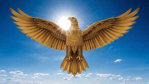 Gilded eagle sculpture spreading wings under sun halo against clear blue sky