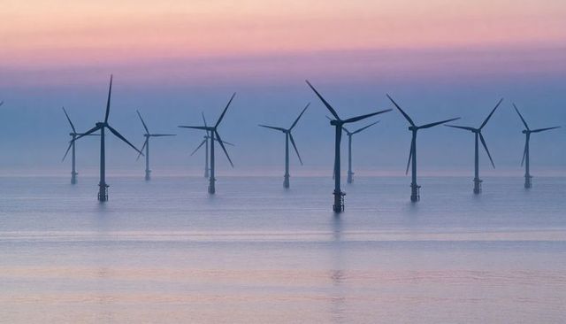 Pastel Sunrise Offshore Wind Farm Silhouettes Over Calm Sea With Misty Horizon
